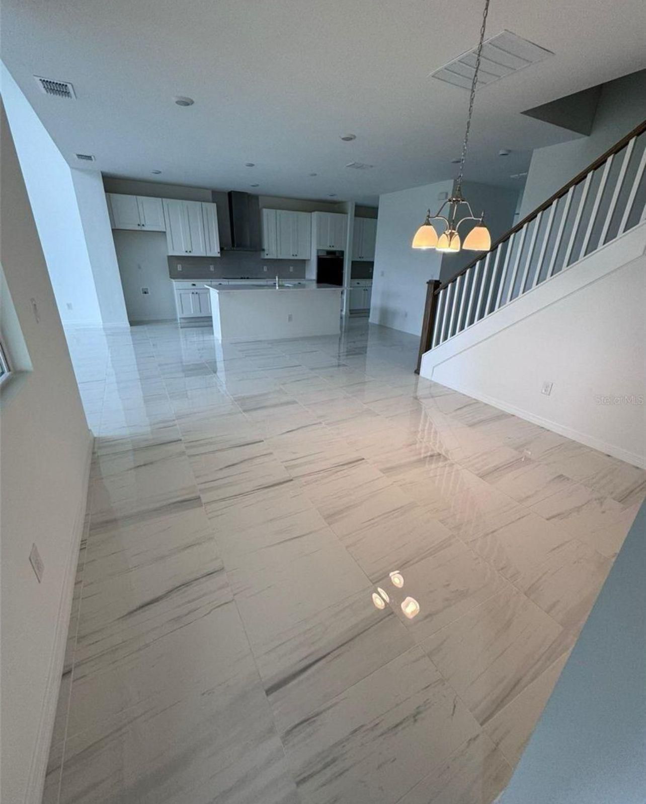 Open-plan great room with glossy marble-look tile and staircase